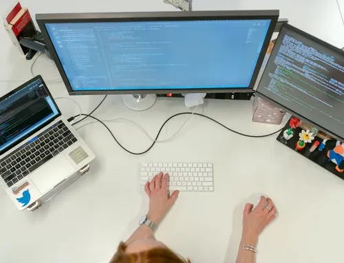 An top view of a woman's desk with 2 monitors and a laptop.