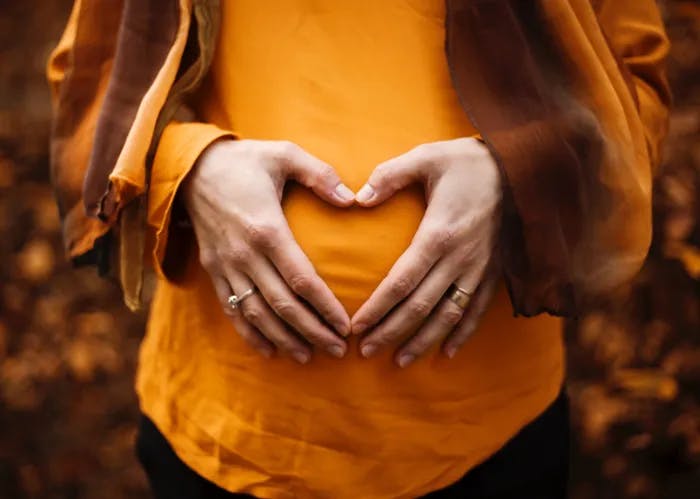 Photo of an expectant mother's hands forming a heart shape over her belly bump