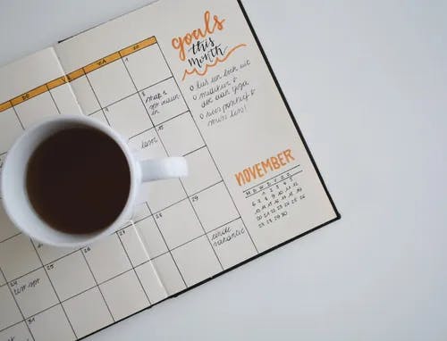A calendar on a table with a coffee mug on top.