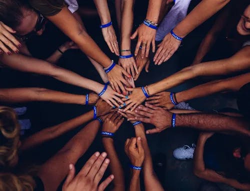 A group of people putting their hands in the center of their group, one on top of each other.